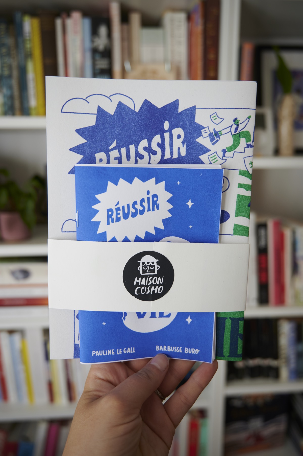 Zine contenant un livret et une affiche imprimée en riso tenue par une bande de carton et un sticker Maison Cosmo